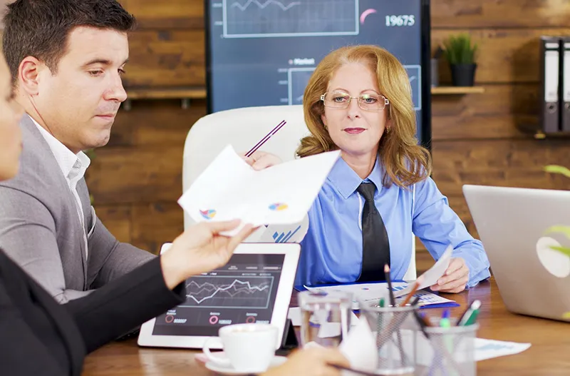 Kadry i płace – zadania działu kadr w nowoczesnym przedsiębiorstwie: trzy osoby podczas spotkania kadrowo-płacowego, analizują wykresy na dokumentach oraz ekranie laptopa